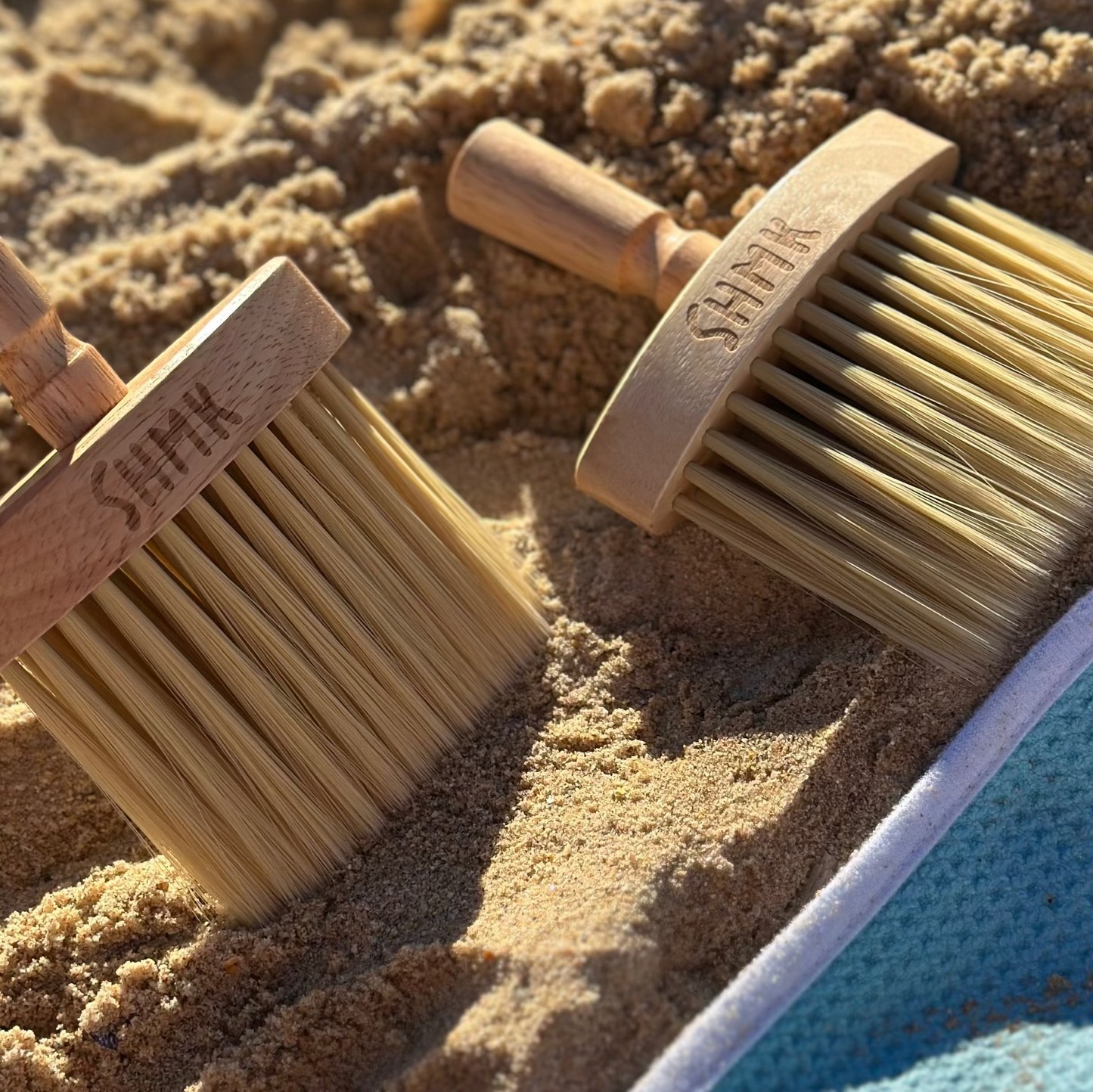 Two sand brushes on the beach with the 'Elitisi towel